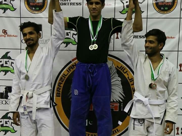 Amjad Khan in a blue gi on top of the podium with his gold medal