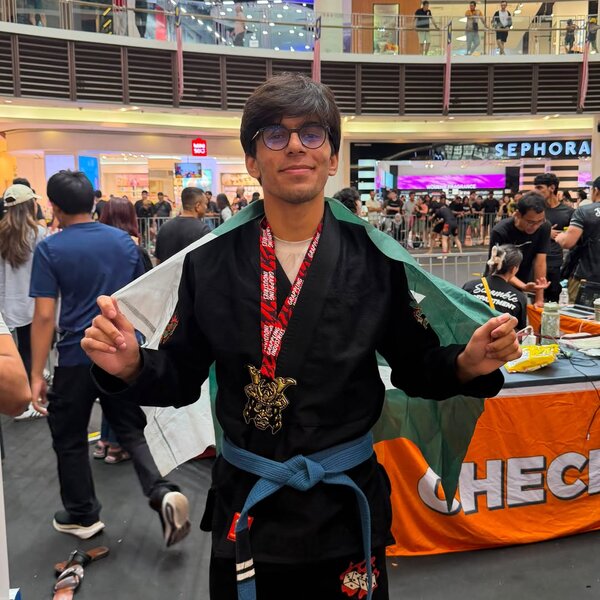 Hashim Ali smiling with a gold medal and the Pakistan flag over his shoulders