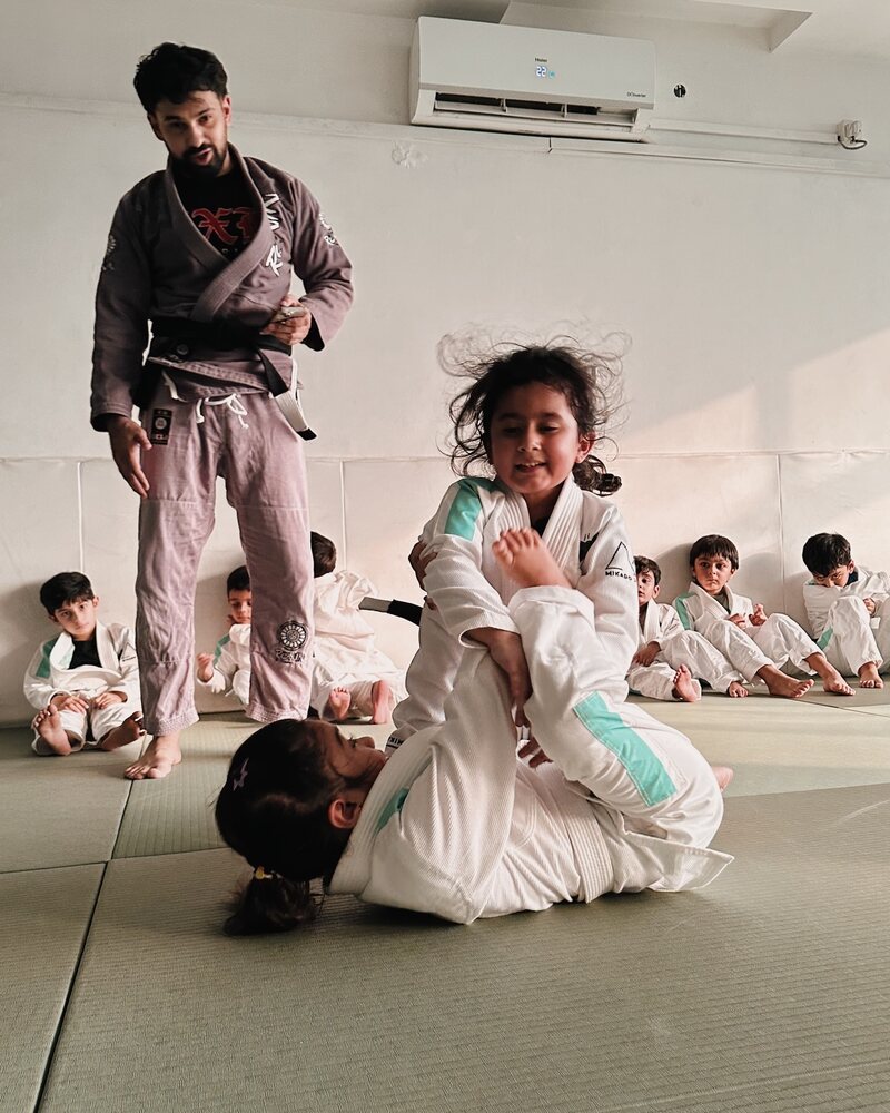 A coach watching two young girls grapple during kids class