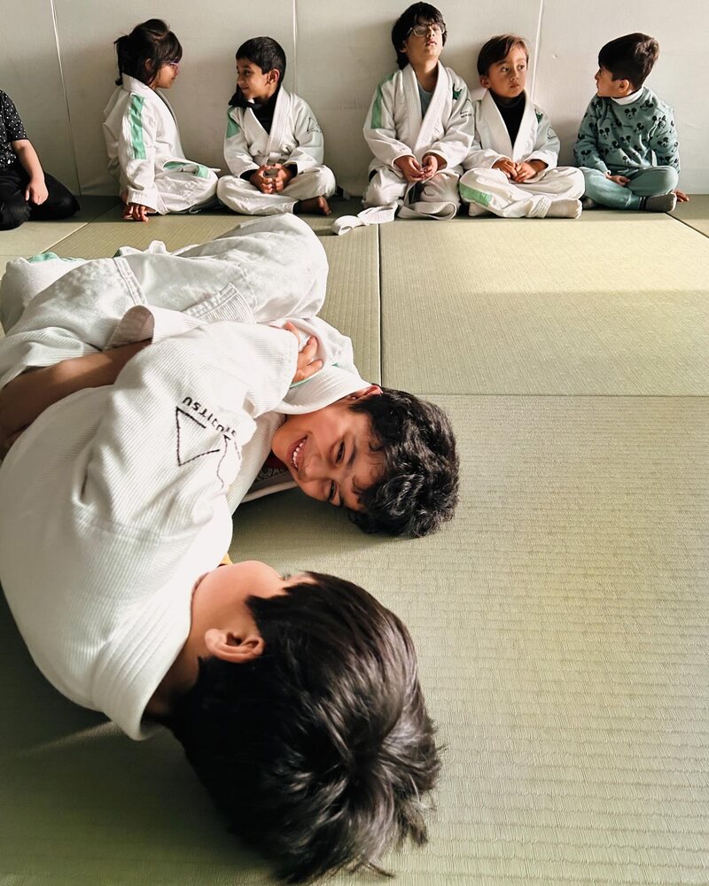 Two boys laughing while they roll, with classmates watching