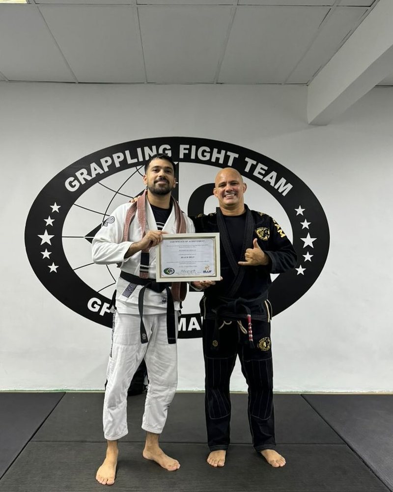 Shaheryar Khalid in a white gi and his new black belt, holding his black belt certificate beside Professor Pedro Falbo at GFTeam Malaysia